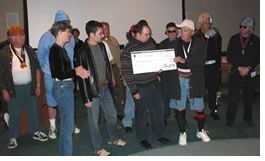 The AIA Board Class of 2002, fresh from their "We Got Mojo" Fun Night rap, present the AIAS officers with a check for $12,000. That's Wayne Silberschlag, AIA, handing it over to Larry Fabbroni.
